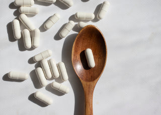 White supplement capsules scattered around a wooden spoon that contains a single capsule.