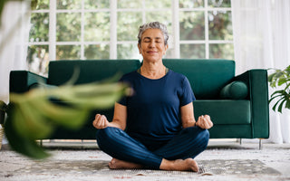 Middle-aged woman in all blue sitting cross-legged in a meditation position in front of a green couch.