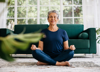 Middle-aged woman in all blue sitting cross-legged in a meditation position in front of a green couch.