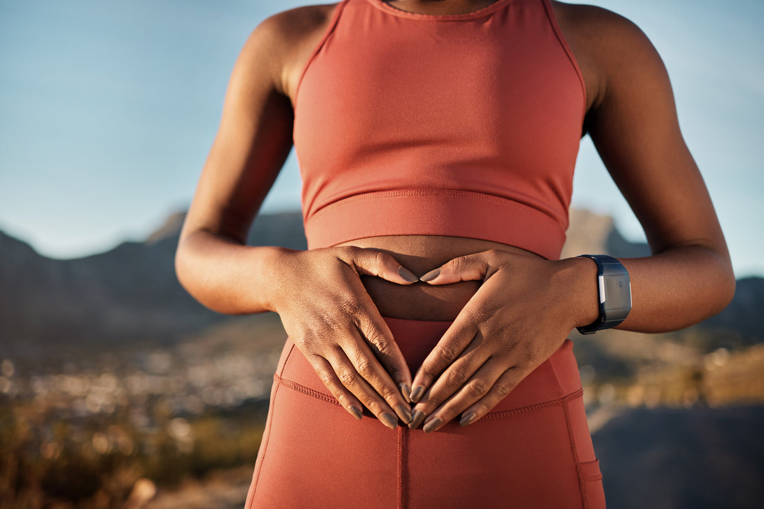 Female in matching pink workout gear standing with the city skyline in the background holding her hands gently over her midsection.