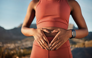 Female in matching pink workout gear standing with the city skyline in the background holding her hands gently over her midsection.