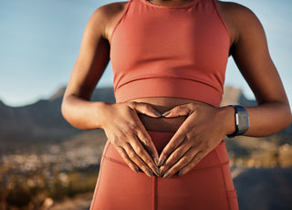 Female in matching pink workout gear standing with the city skyline in the background holding her hands gently over her midsection.