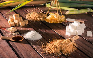 An array of different types of sugars, including brown sugar, honey clumps, and sugar cubes, sitting on a wooden table.