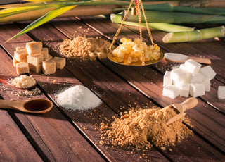 An array of different types of sugars, including brown sugar, honey clumps, and sugar cubes, sitting on a wooden table.