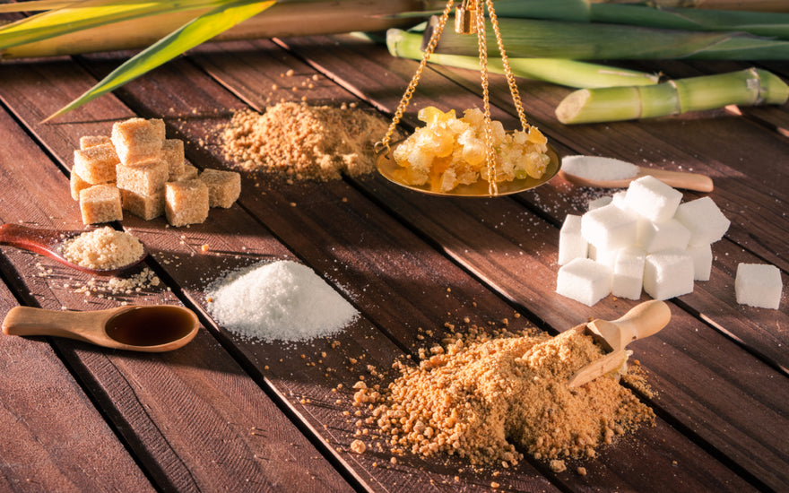 An array of different types of sugars, including brown sugar, honey clumps, and sugar cubes, sitting on a wooden table.