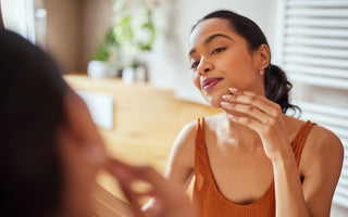 Woman standing in front of a mirror examining the skin on her face.