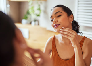 Woman standing in front of a mirror examining the skin on her face.