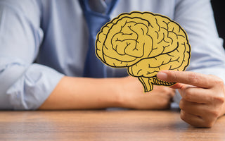 Person sitting at a table holding a yellow piece of paper with a brain drawn on it.