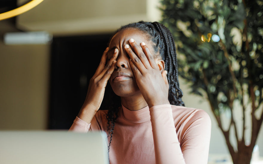 Tired young woman covering her eyes with her hands while sitting in front of her laptop.