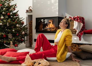 Young adult women in red pants and a yellow sweater relaxing on the floor in front of a Christmas tree. 