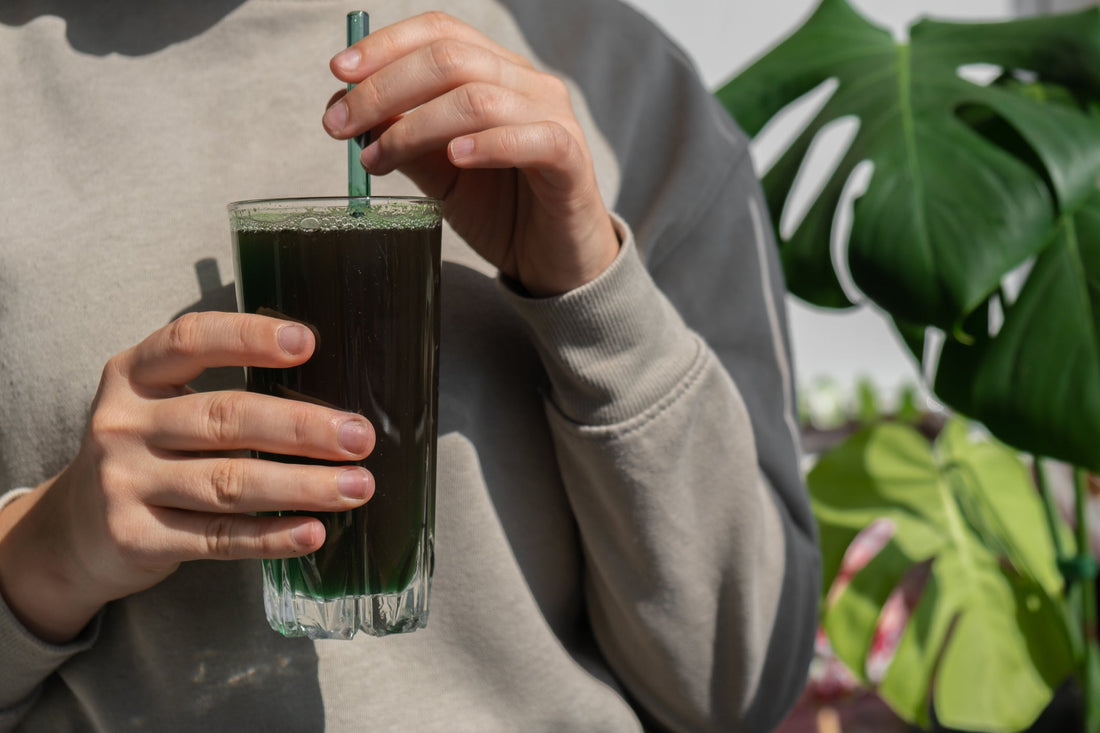 Female hands holding organic blue-green algae drink in a glass.