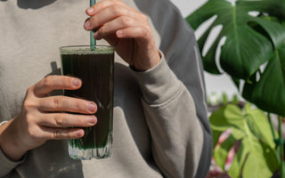 Female hands holding organic blue-green algae drink in a glass.