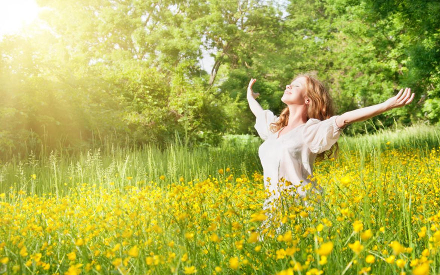 Young female standing in a green field with tall grass with her head titled up and her arms spread out to the side.