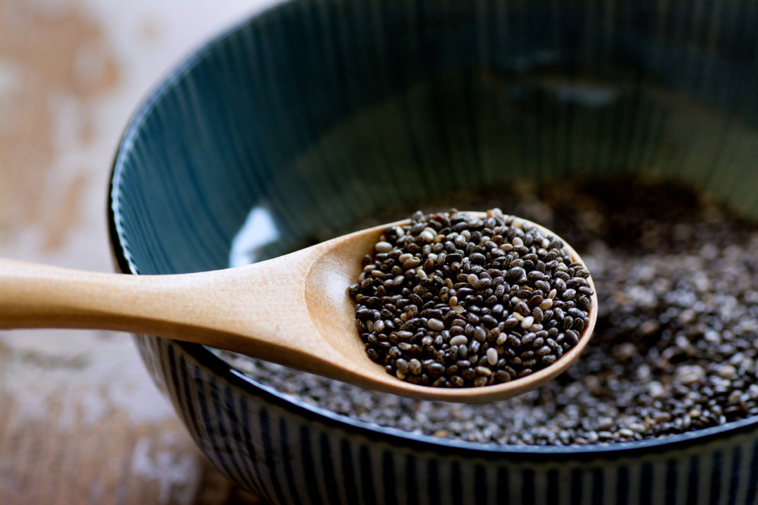 Wooden spoon scooping chia seeds out of a dark ceramic bowl.