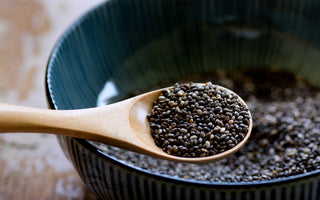 Wooden spoon scooping chia seeds out of a dark ceramic bowl.