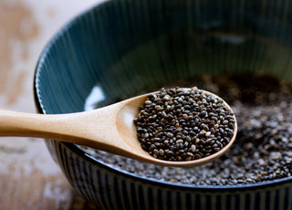 Wooden spoon scooping chia seeds out of a dark ceramic bowl.