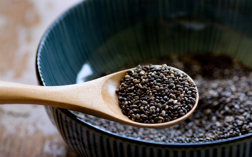 Wooden spoon scooping chia seeds out of a dark ceramic bowl.