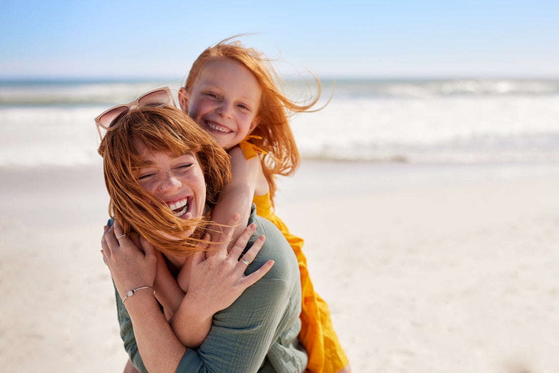 Joyful young mother smiling with her daughter on her back at the beach.
