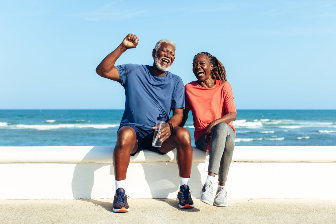 Joyful senior couple wearing exercise clothes laughing together on a sunny seaside promenade. 