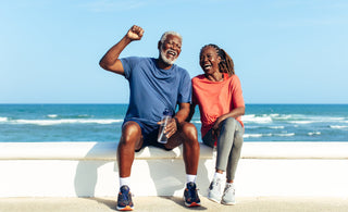 Joyful senior couple wearing exercise clothes laughing together on a sunny seaside promenade. 