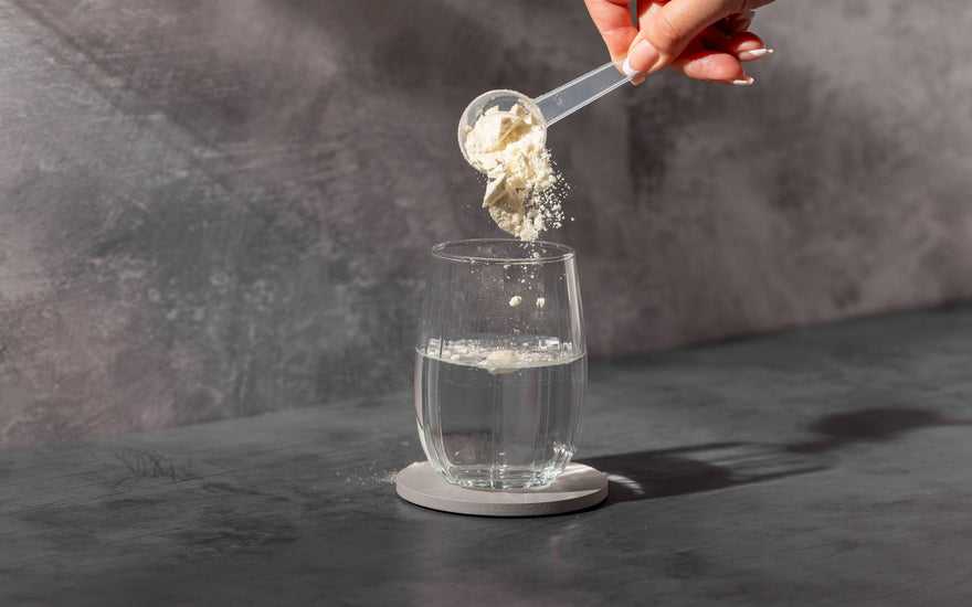 Pouring white powder supplement into a glass of water. 
