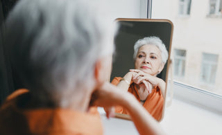 Senior female with short gray hair looking solemnly at her reflection in a mirror.  