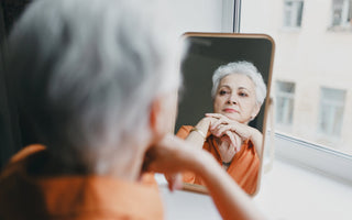 Senior female with short gray hair looking solemnly at her reflection in a mirror.  