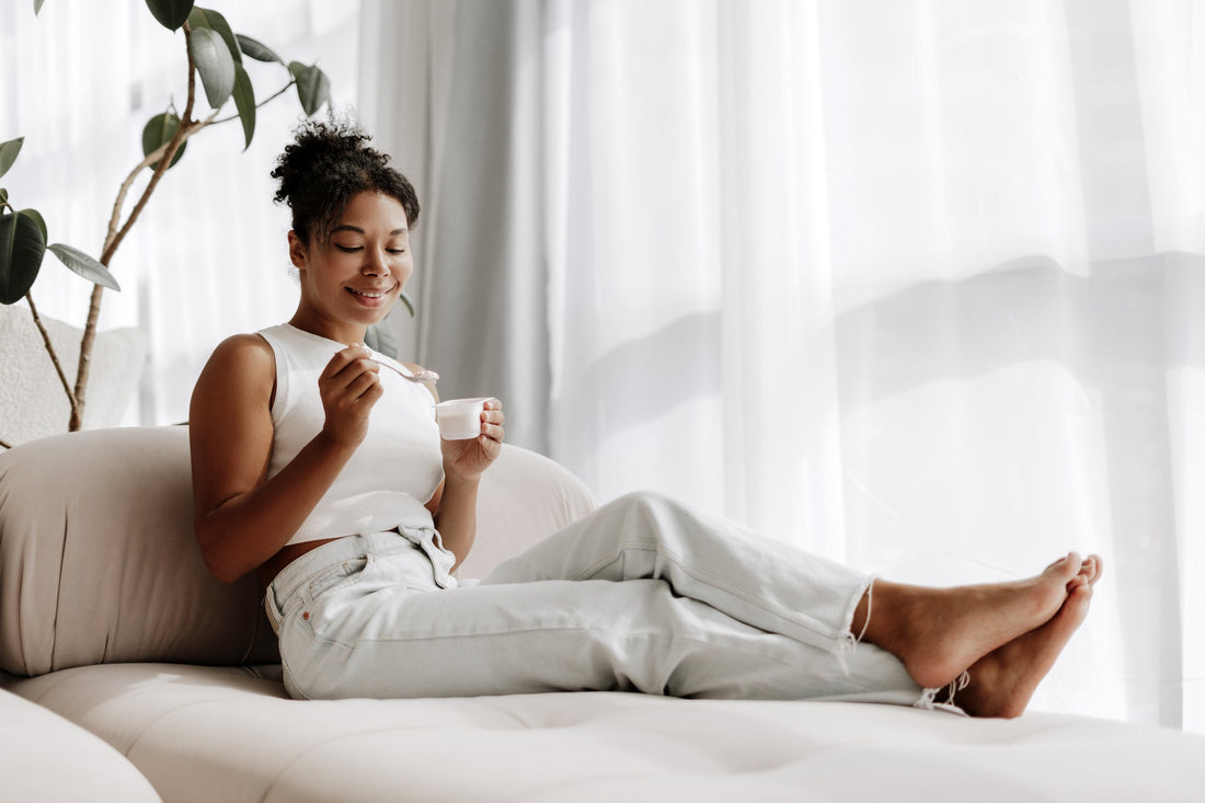 Young woman enjoying yogurt while sitting on her couch at home. 