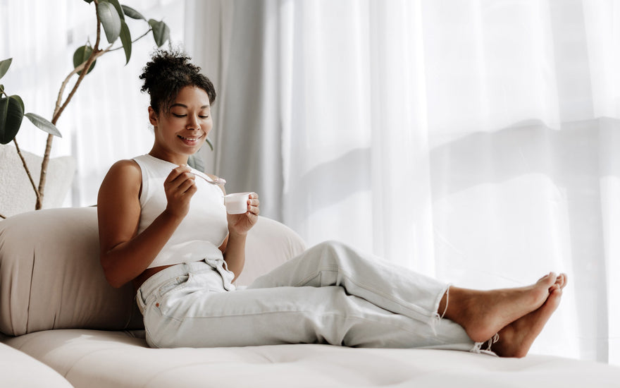 Young woman enjoying yogurt while sitting on her couch at home. 