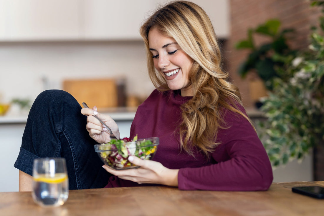 Beautiful smiling woman eating a healthy salad while sitting in her kitchen.