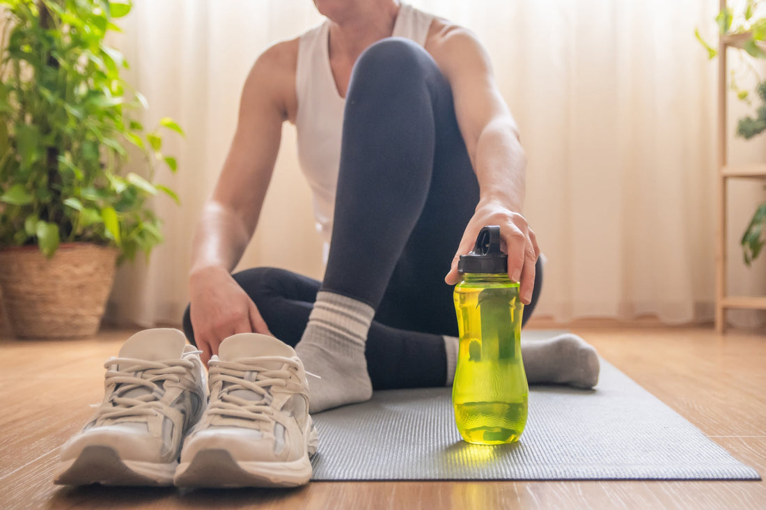 Mature woman relaxing on an exercise mat after completing a home workout, reaching for her electrolyte water bottle to stay hydrated and support her healthy lifestyle