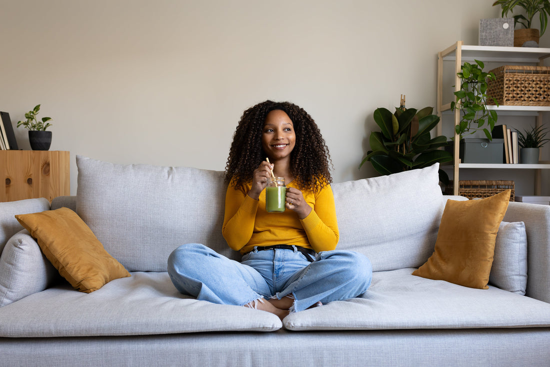 Young woman relaxing on sofa drinking green smoothie at home.