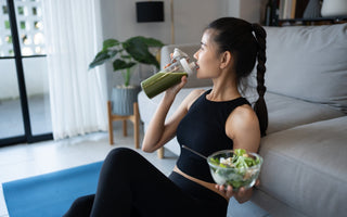 Happy woman in athletic clothing eating a healthy salad and drinking a green smoothie. 