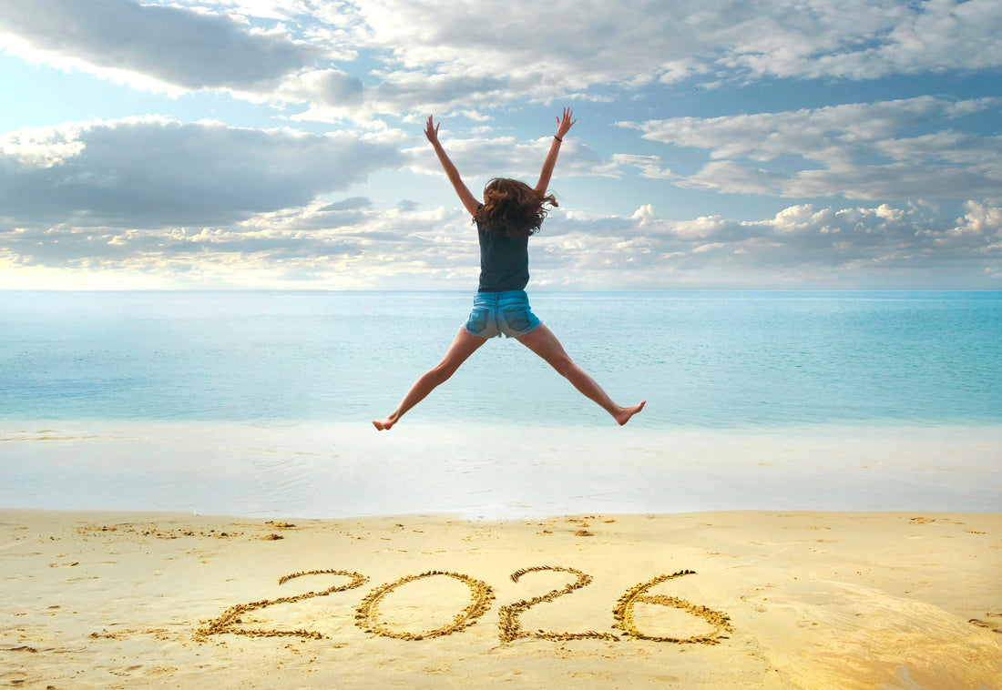 2026 written on sand in front of a happy girl jumping in the air.