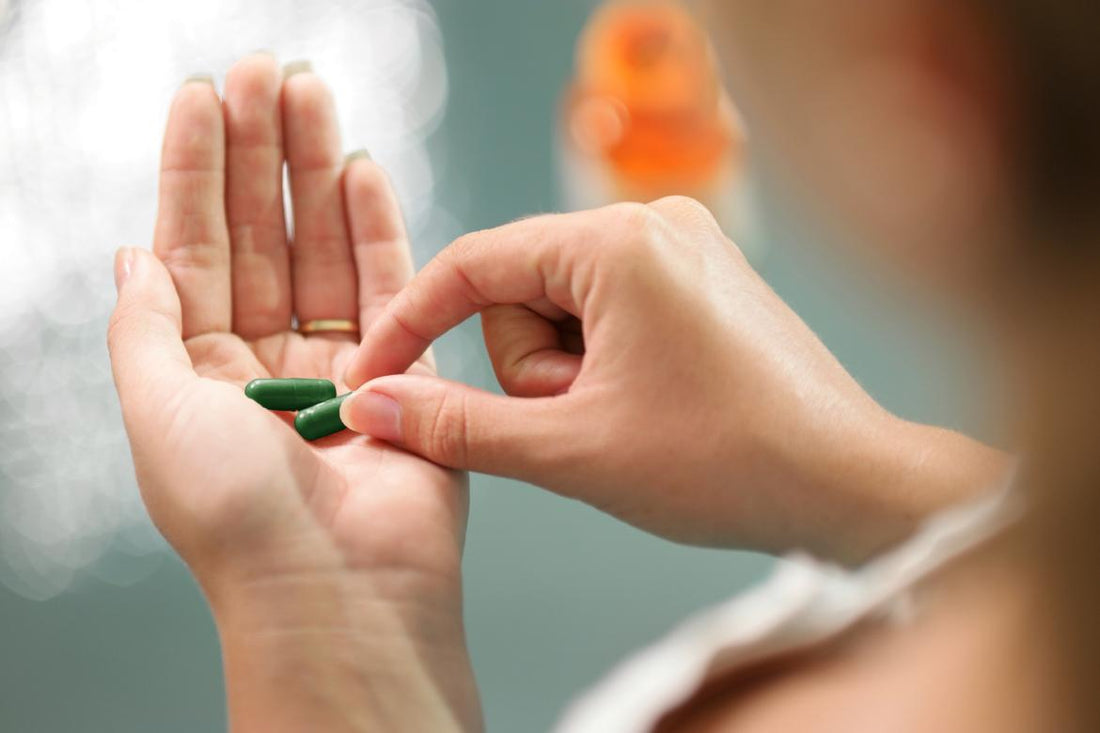 Female grabbing one of two green supplements out of the palm of her left hand.