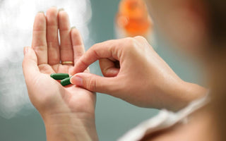 Female grabbing one of two green supplements out of the palm of her left hand.