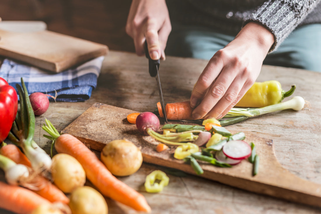 Two hands chopping a carrot on a wooden cutting board.