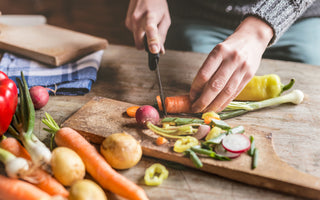 Two hands chopping a carrot on a wooden cutting board.