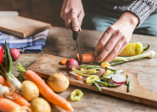 Two hands chopping a carrot on a wooden cutting board.