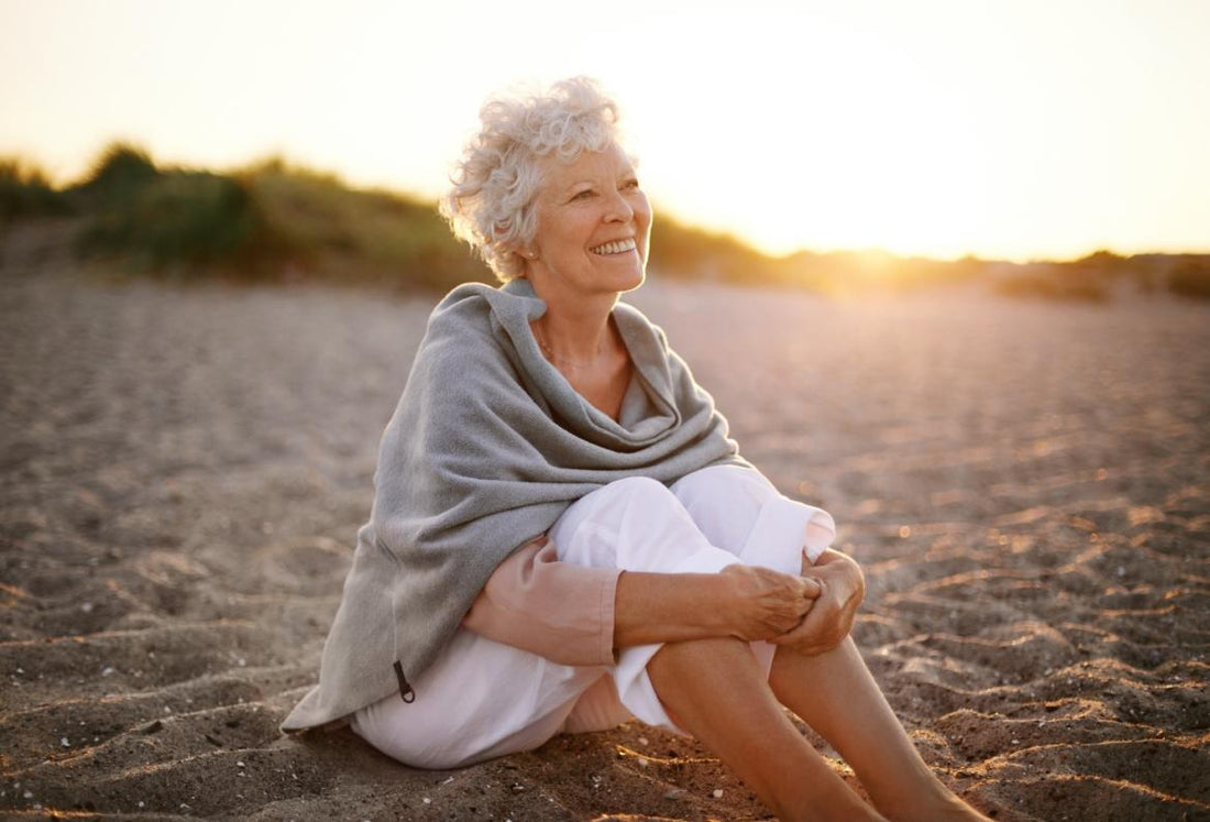Elderly woman with short white hair sitting in the sand at the beach watching the sunset.