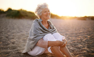 Elderly woman with short white hair sitting in the sand at the beach watching the sunset.