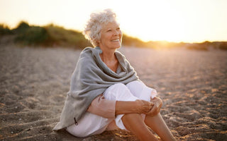 Elderly woman with short white hair sitting in the sand at the beach watching the sunset.