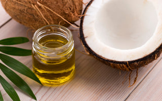 Half of a coconut sitting next to a mason jar of coconut oil on a wooden tabletop.