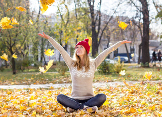 Happy woman sitting in the ground, throwing leaves into the air.