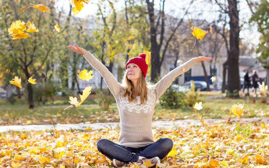 Happy woman sitting in the ground, throwing leaves into the air.