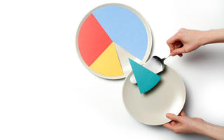 Hands using a pie server to transfer a piece of colored paper from a pie chart to a plate.