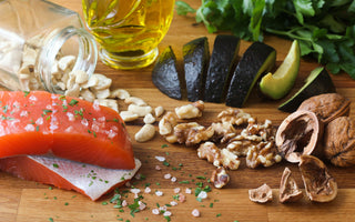 An array of healthy fatty foods like salmon and avocados on a wooden tabletop. 