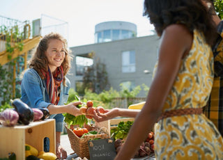 Local farmer smiling while handing fresh produce to a pair of customers at the farmers market.