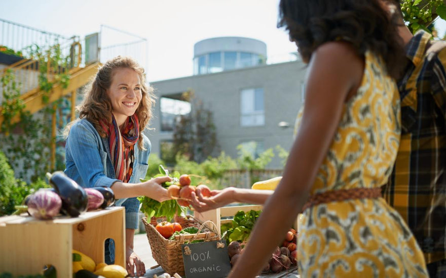 Local farmer smiling while handing fresh produce to a pair of customers at the farmers market.