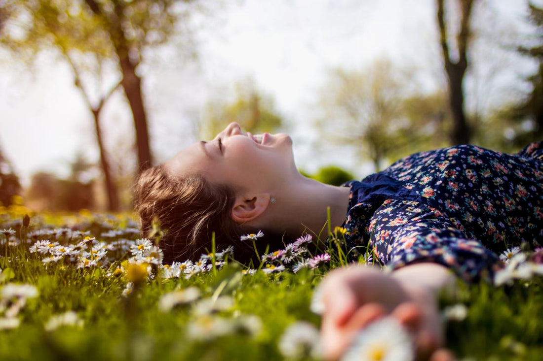 Young woman laying in the grass smiling and soaking up the sun. 